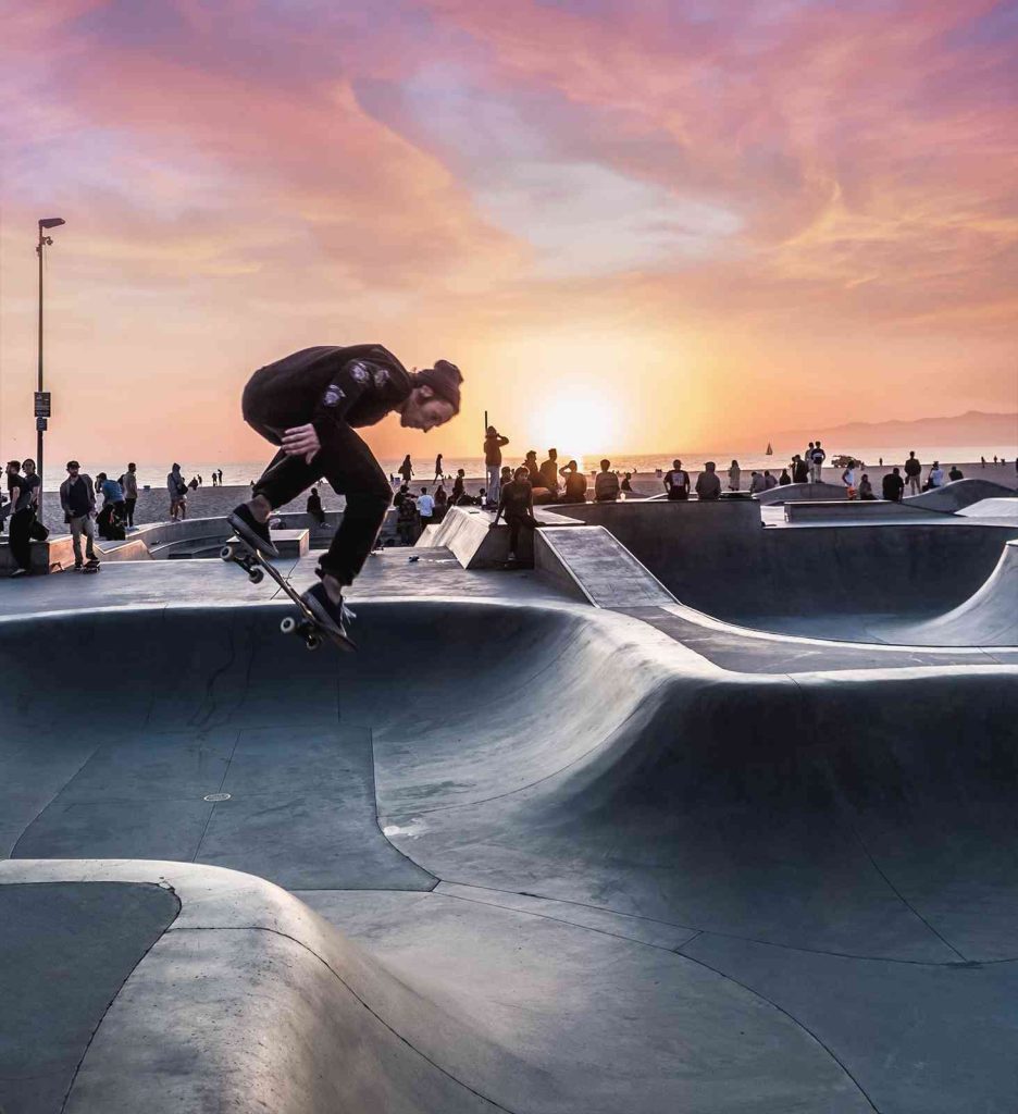 Skateboarder performing trick at a skatepark during sunset.